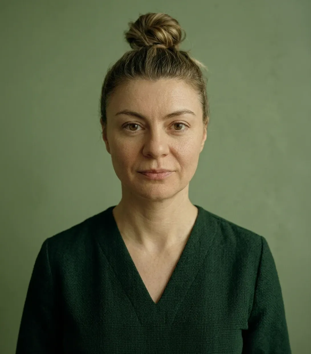 Green-toned editorial studio portrait of a woman with her hair in a bun, featured on the WeGrow site.